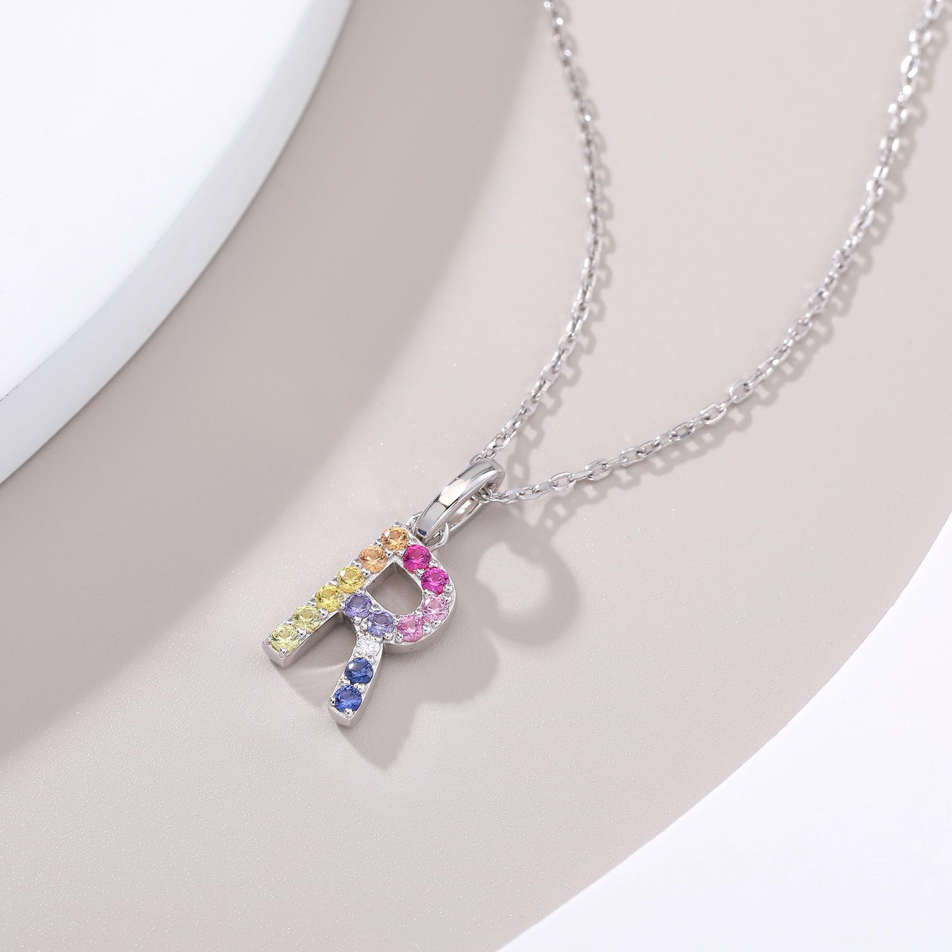 A delicate sterling silver initial necklace holding an uppercase letter R pendant meticulously set with a multi-color rainbow spectrum of round lab sapphires.