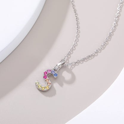 A delicate sterling silver initial necklace showcasing a fluid, serpentine letter S pendant precision-set with a continuous rainbow wave of vibrant round lab sapphires.