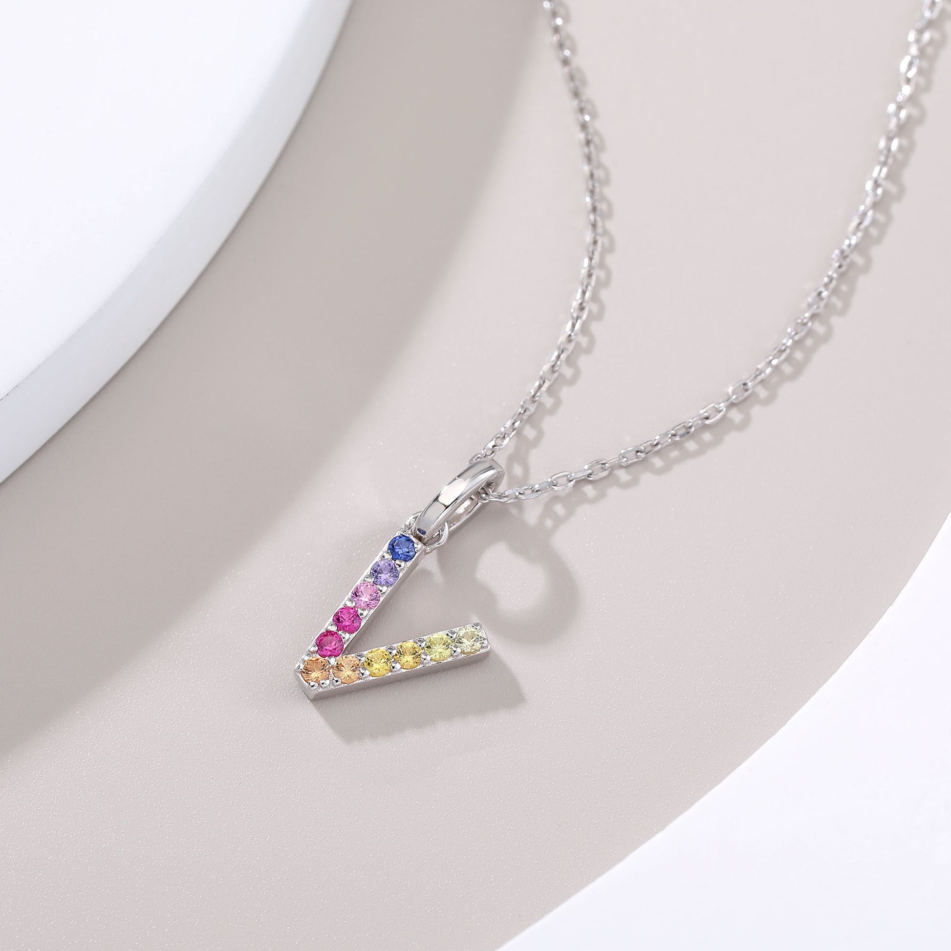 A delicate sterling silver cable chain necklace showcasing an architectural capital letter V pendant precision-set with a dynamic rainbow gradient of multi-color lab sapphires.