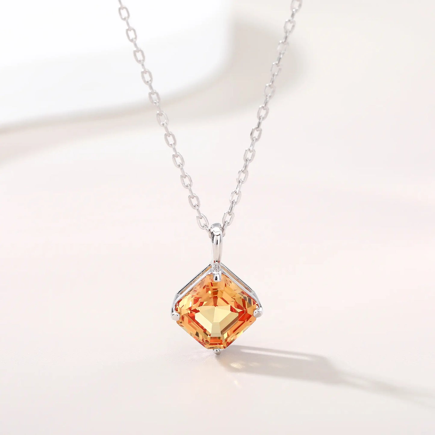 An elegant Asscher cut sapphire pendant necklace in champagne yellow, secured in a four-prong sterling silver setting with a delicate chain and reflective shadow below.