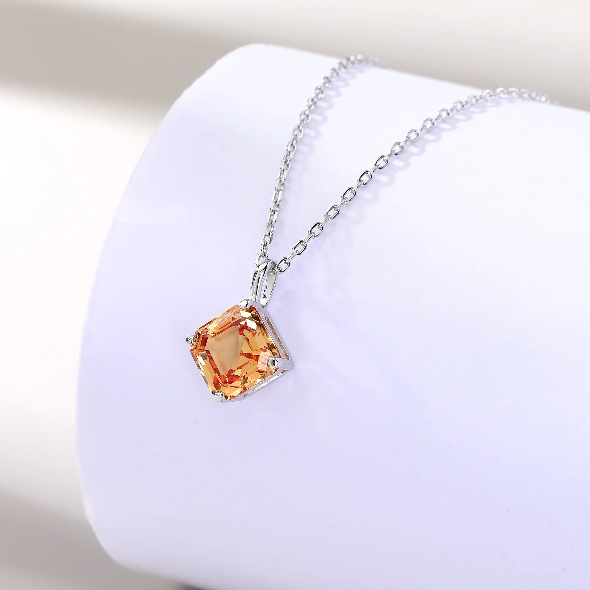 An elegant Asscher cut sapphire pendant necklace in champagne yellow, secured in a four-prong sterling silver setting with a delicate chain and reflective shadow below.