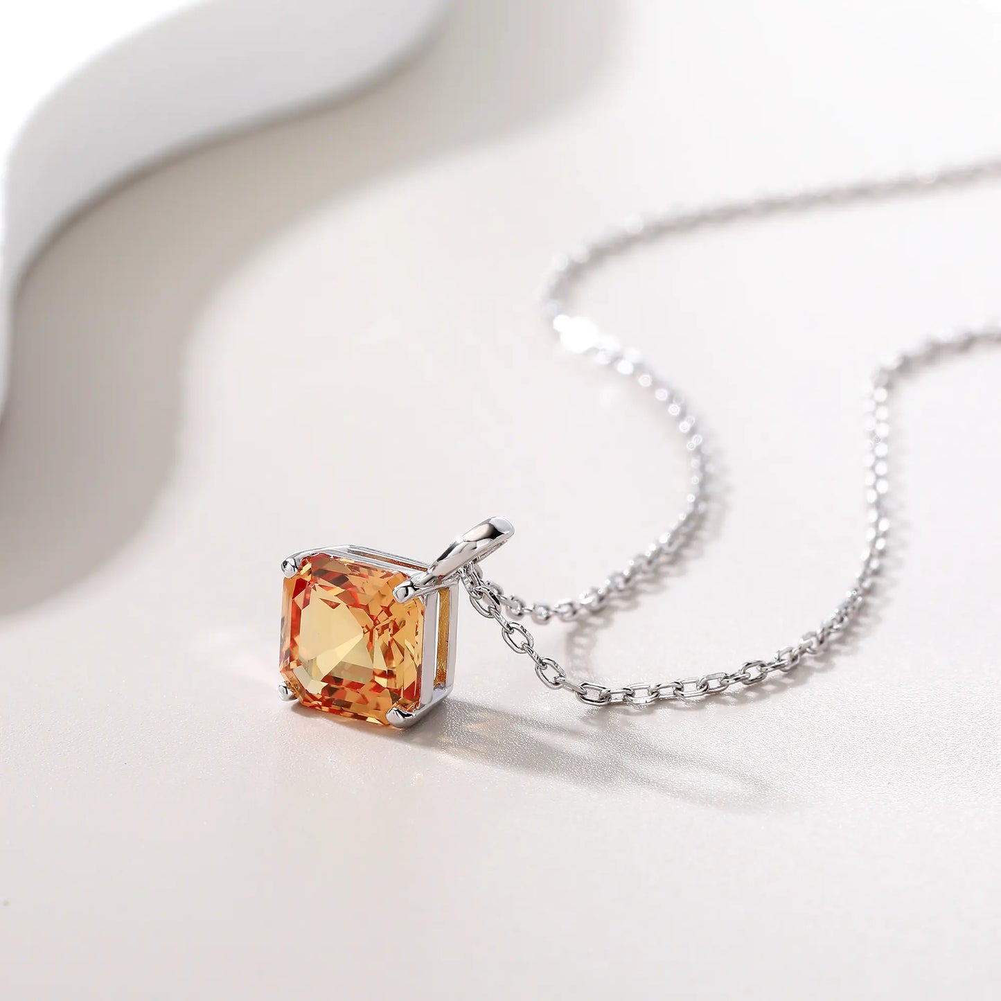 An elegant Asscher cut sapphire pendant necklace in champagne yellow, secured in a four-prong sterling silver setting with a delicate chain and reflective shadow below.