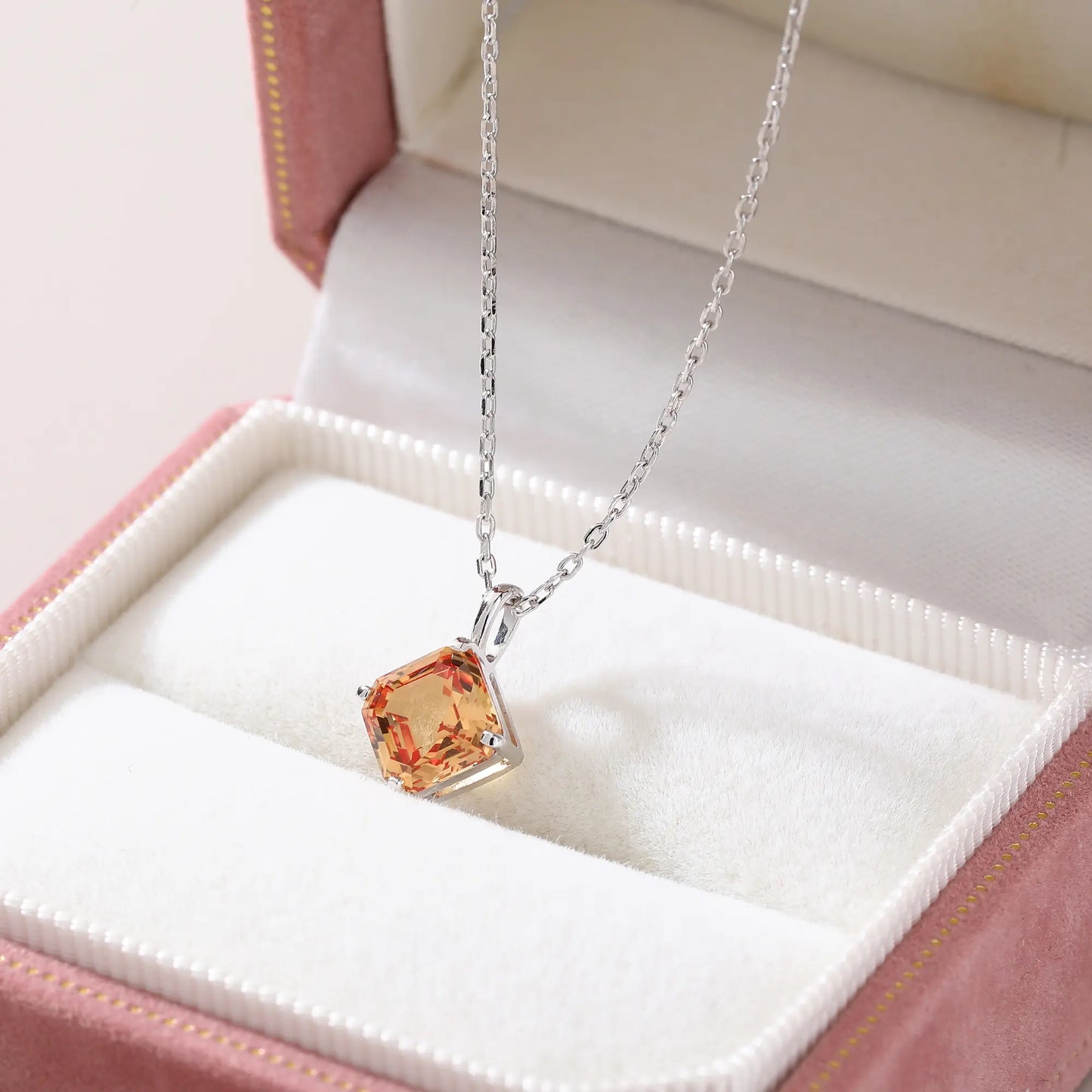 An elegant Asscher cut sapphire pendant necklace in champagne yellow, secured in a four-prong sterling silver setting with a delicate chain and reflective shadow below.